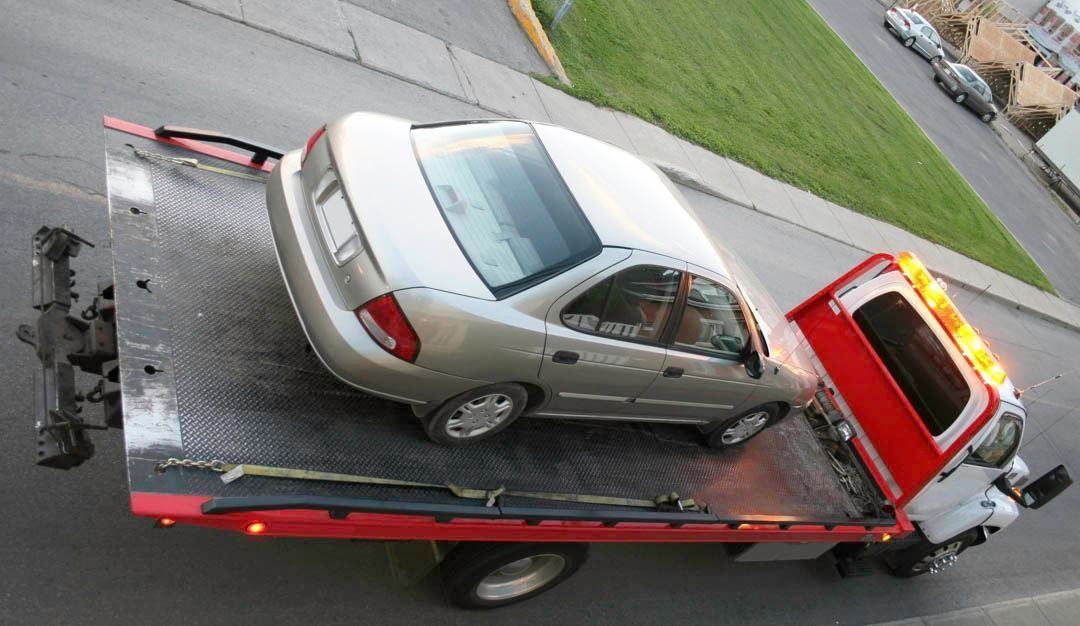 Silver sedan being towed on a flatbed tow truck; roadside setting.