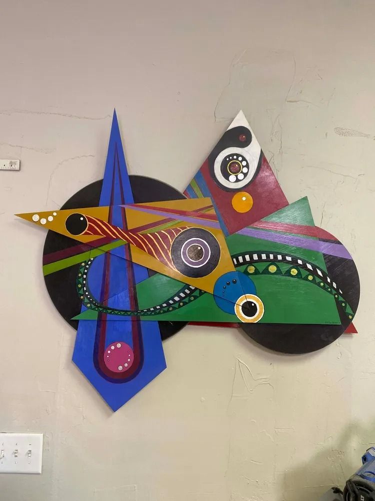 Abstract geometric artwork in primary colors, with circles, triangles, and lines, mounted on a wall.