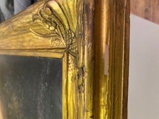 Close-up of a gold ornate picture frame corner with chipped paint, revealing a dark painting within.