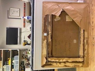 Back of an artwork with a torn paper backing, revealing the wood frame and some handwritten labels.