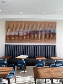 Wooden tables with blue chairs, long blue bench seating against a white wall with a large abstract art piece.