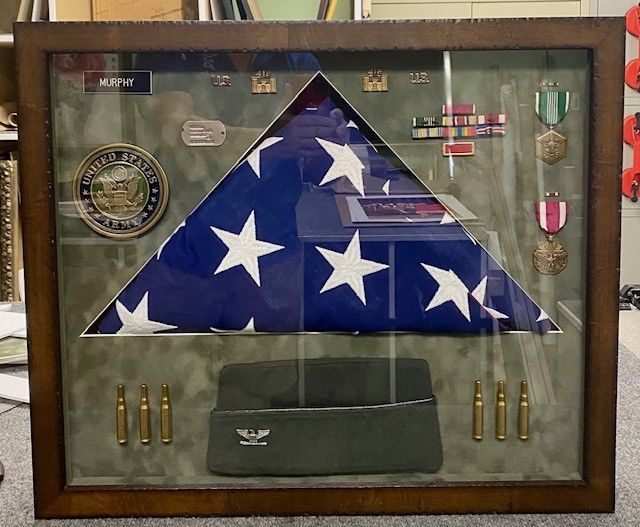 Shadowbox display: folded American flag, medals, cap, and bullets; all in a wooden frame. Military service memorial.