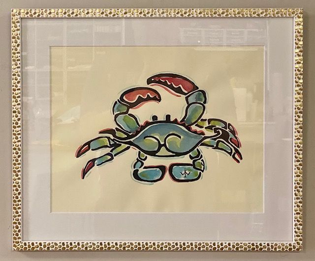 Framed watercolor painting of a blue crab with red claws on a cream background. The frame is white with a patterned border.
