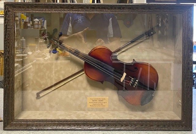 Violin and bow displayed in a shadow box. The violin is brown with a bow across it, in a frame with a beige backing.