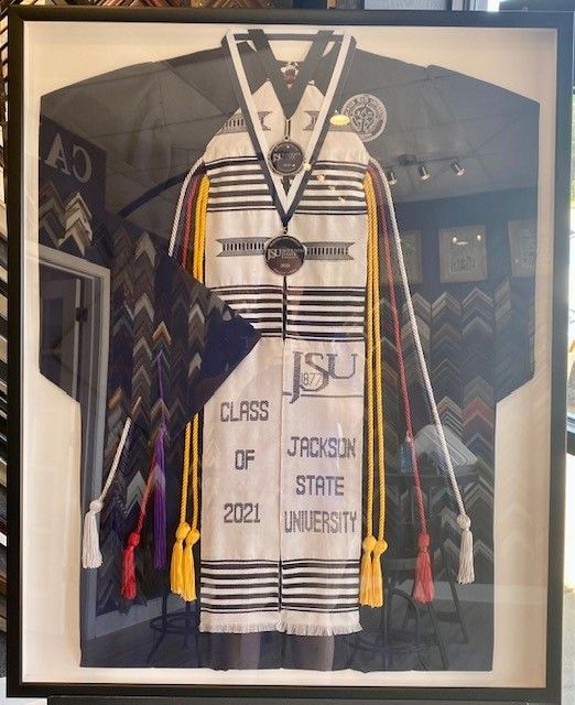 Shadow box with Jackson State University graduation regalia: stole, cords, and medals. Dark frame.