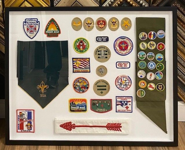 Framed display of Boy Scout patches, badges, and a neckerchief on a white background.