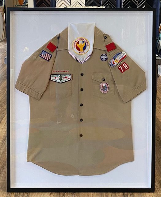 A framed Boy Scout uniform shirt with patches, a neckerchief, and a black frame on a white background.