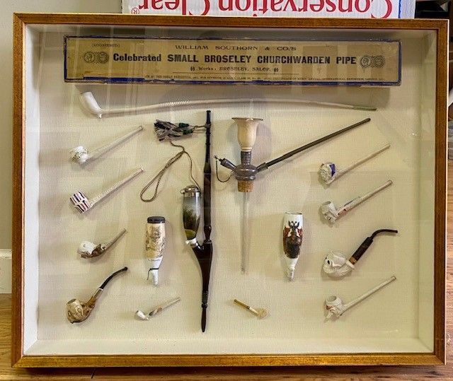 Display case holding various vintage tobacco pipes and a box labeled 