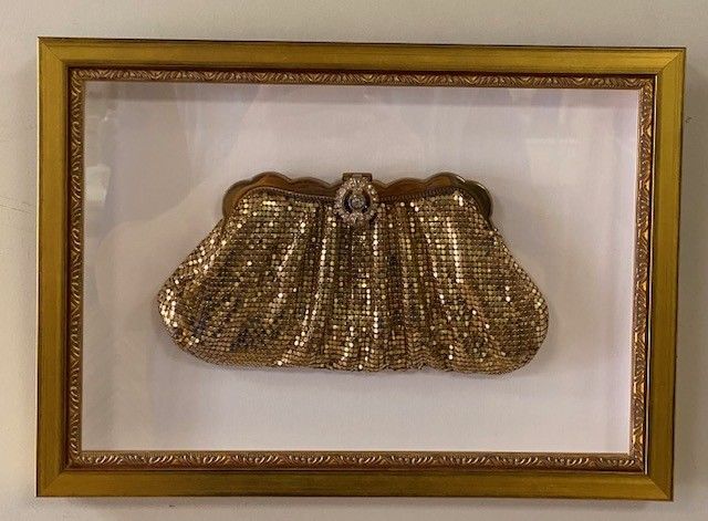 Gold beaded clutch purse framed in a gold rectangular frame on a white wall.