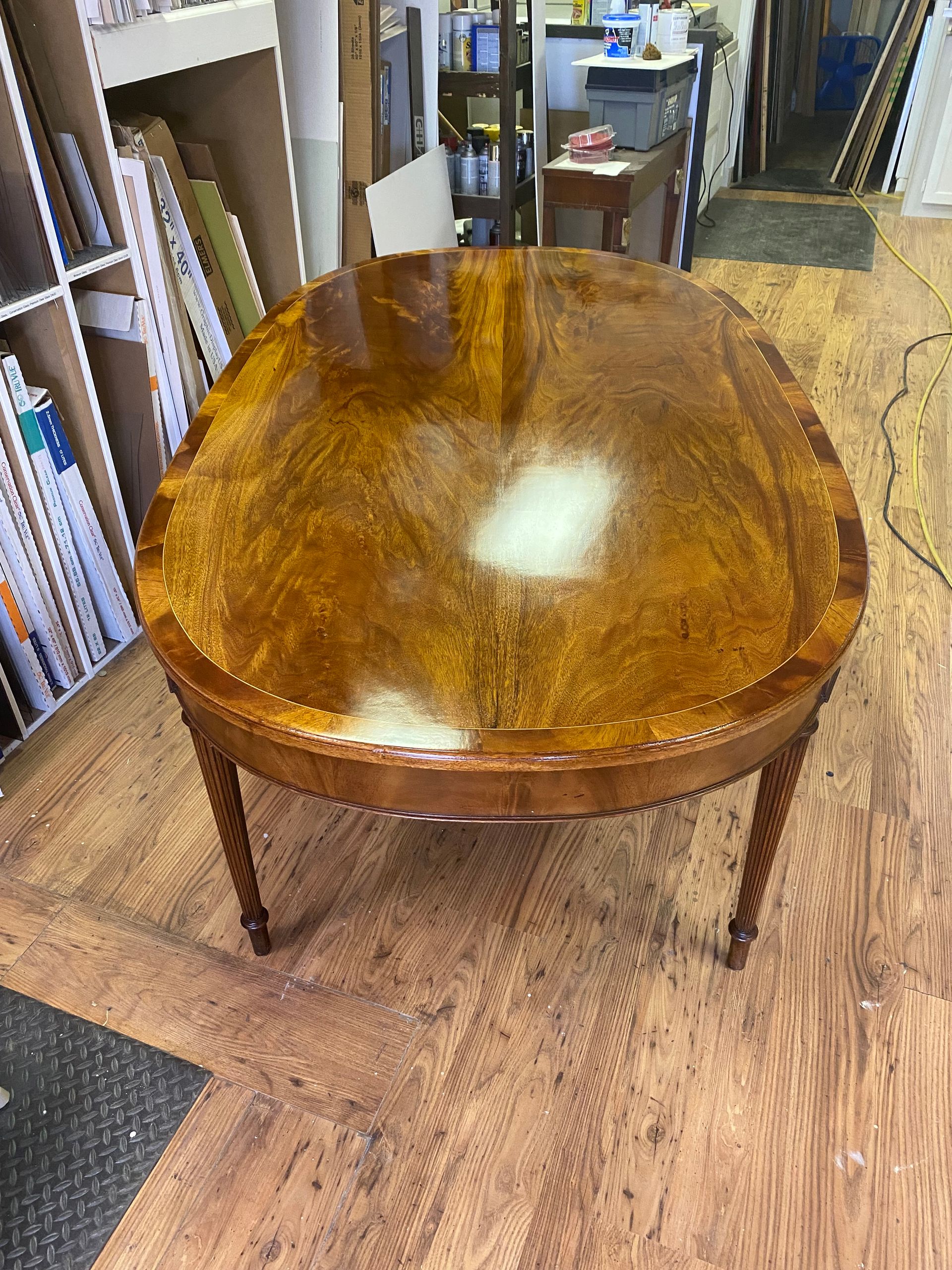 A polished wooden oval table with intricately carved legs, set on a wooden floor in a workshop.
