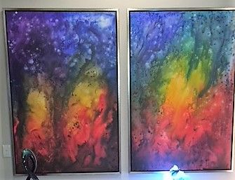 Two framed abstract paintings with a rainbow of colors blending against a dark background.