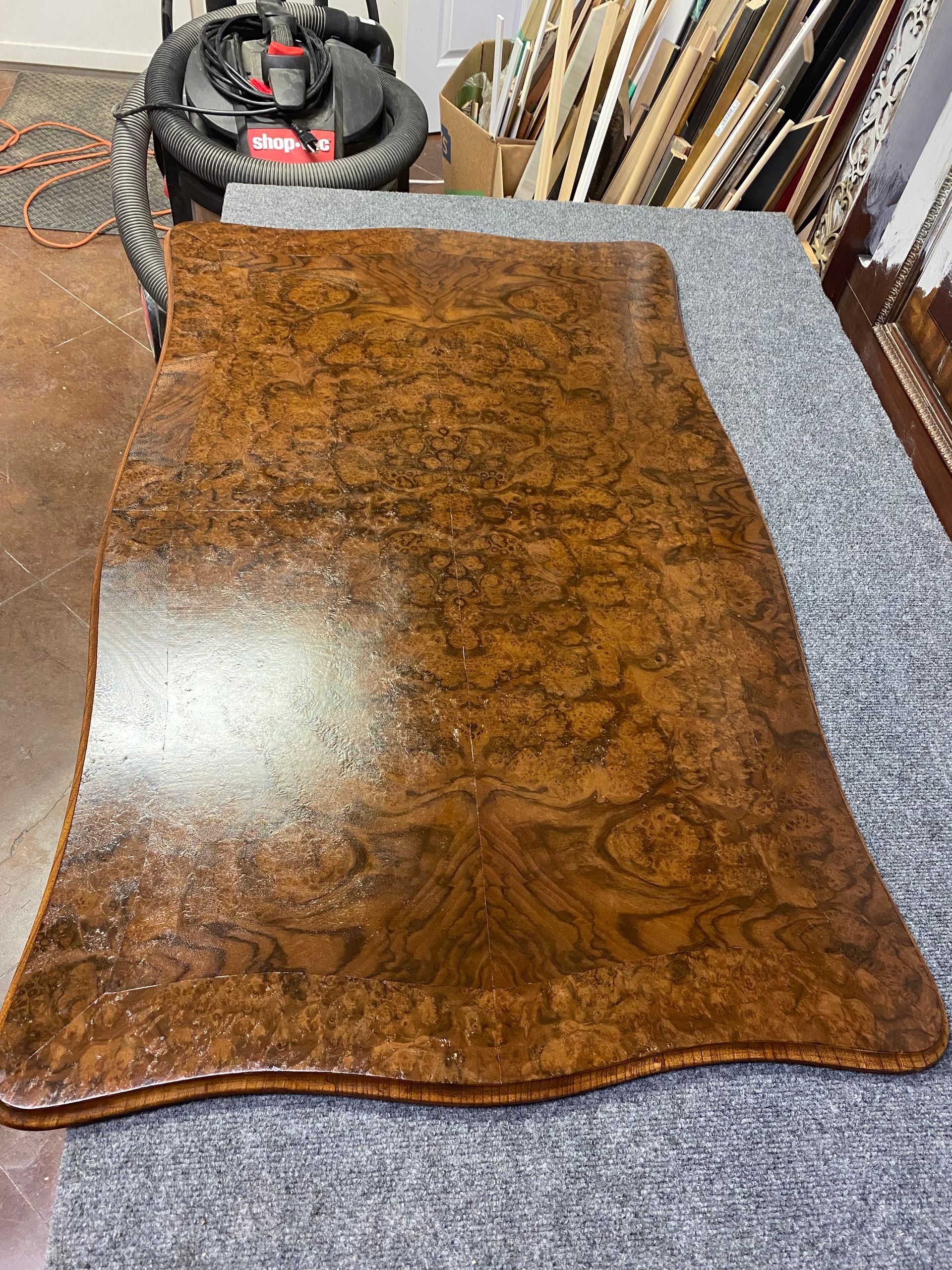 A varnished wood table top with a unique grain pattern rests on a gray surface.