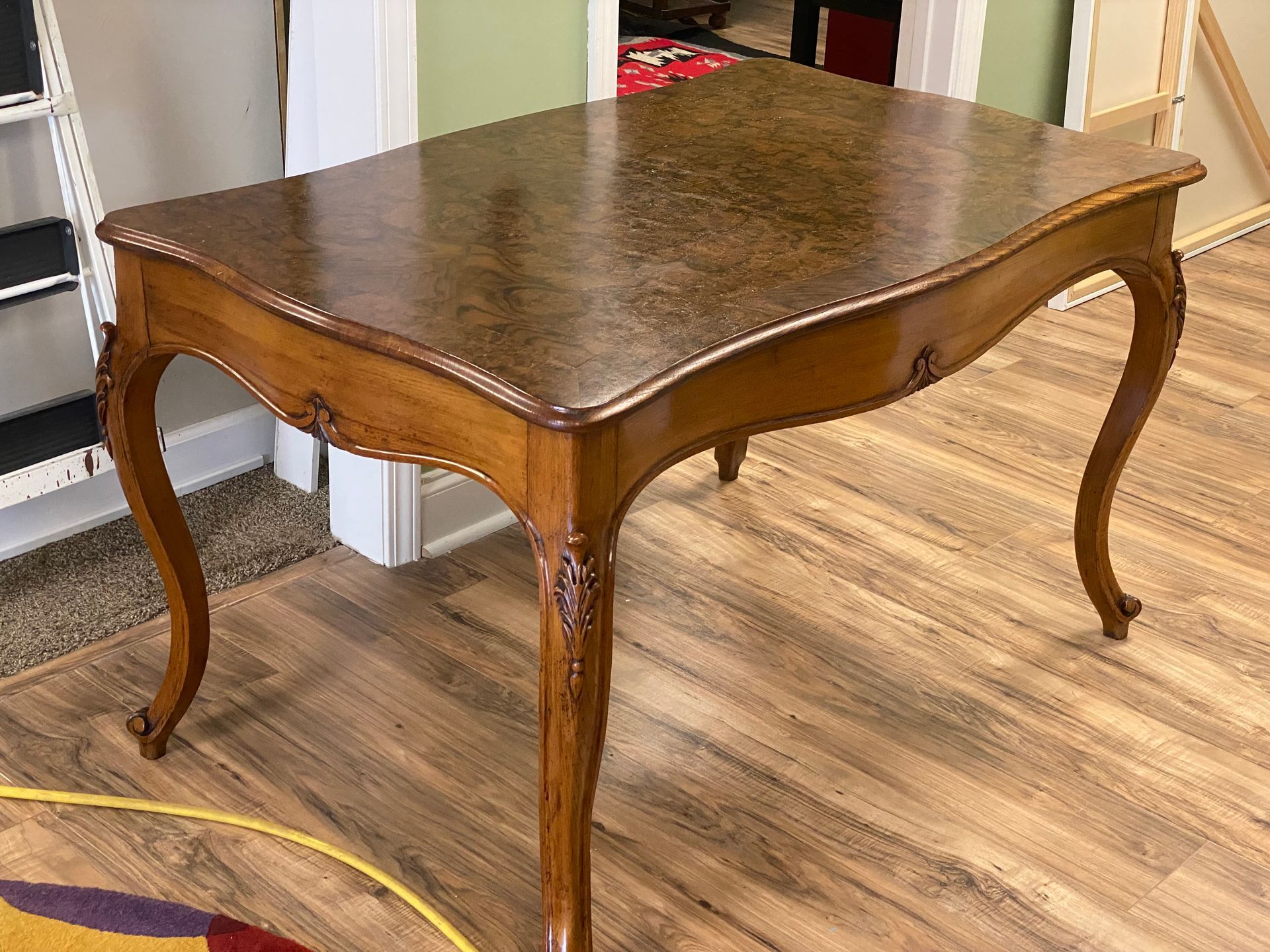 Wooden table with curved legs and a patterned top in a room with hardwood floors.