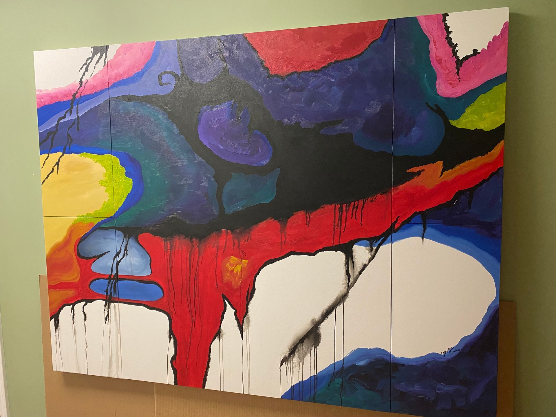 Abstract painting with vibrant colors like red, blue, and yellow, with dripped paint effects, mounted on a wall.