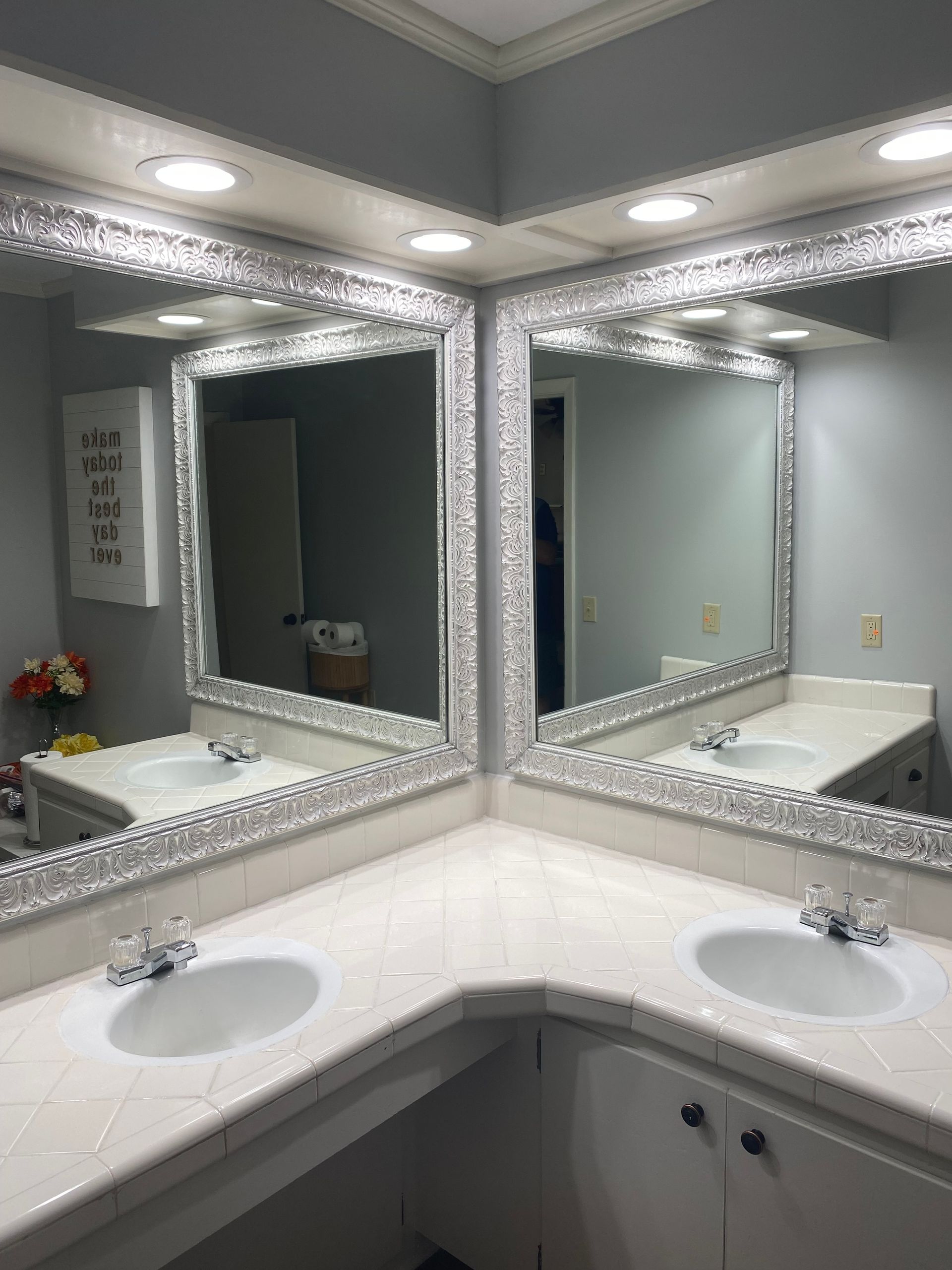 Bathroom with corner vanity, two sinks, and mirrors with crystal trim. Bright lighting.