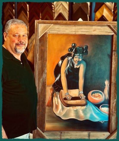 Man beside a painting of an Indigenous woman grinding food, wearing a black dress and hair tied up, brown and orange setting.