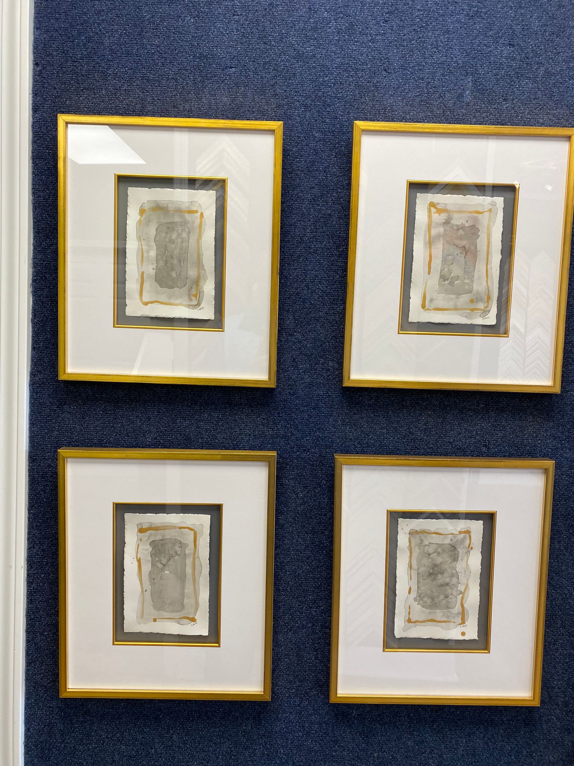 Four framed artworks with gold frames hang on a blue textured wall. 