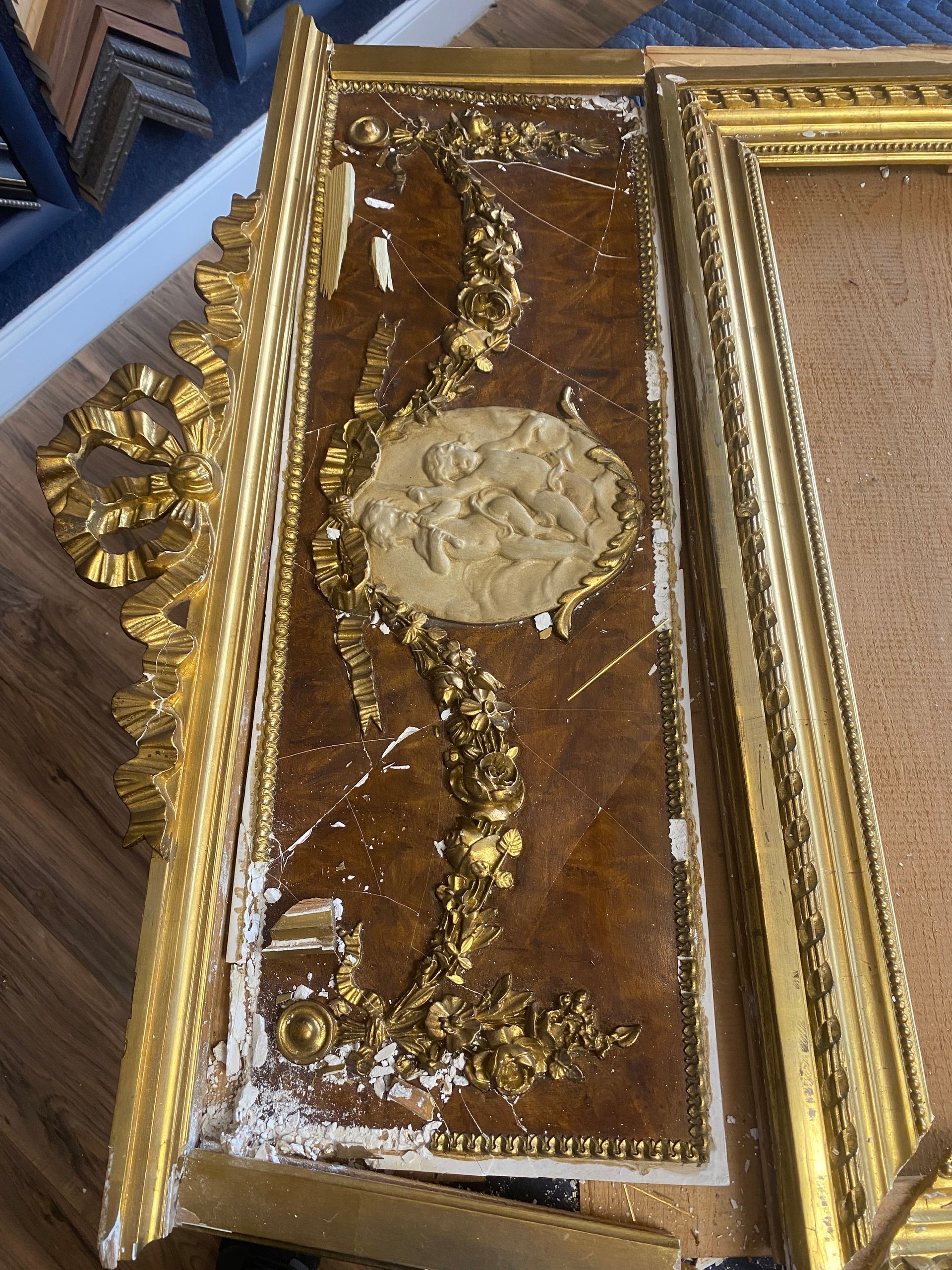 Close-up of a damaged gold picture frame with ornate, raised gold detailing on a textured brown background.