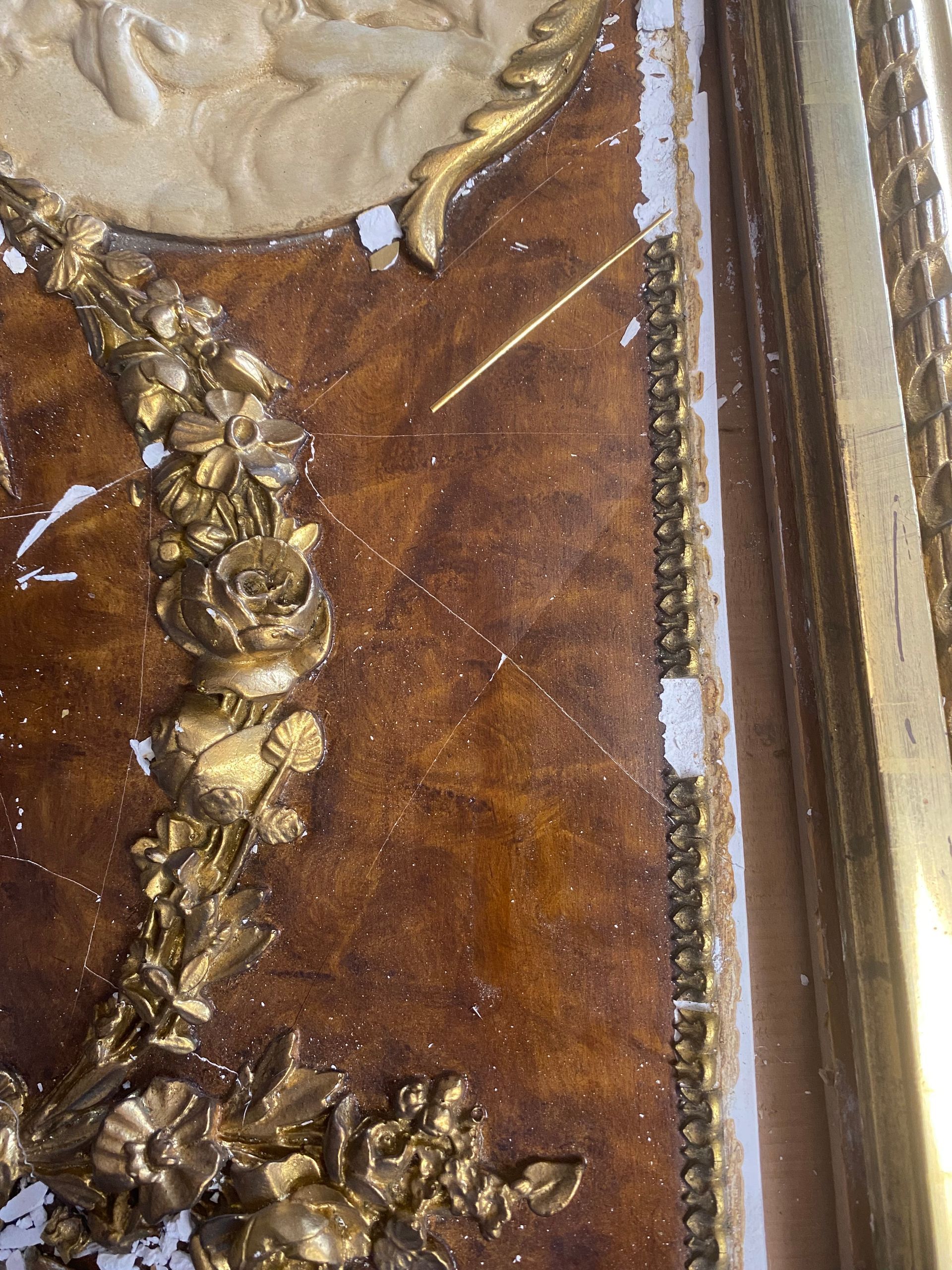 Close-up of ornate, golden frame with a faux-marbled, brown surface and floral embellishments.  Some paint is chipped.