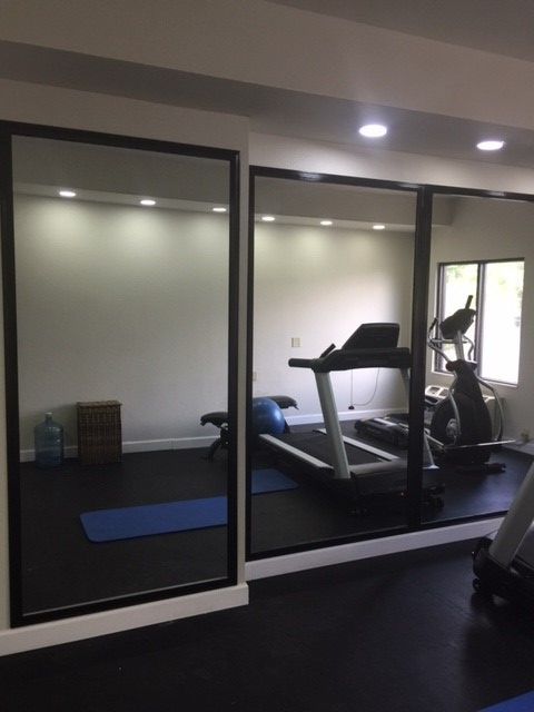 Mirrored home gym with treadmill, exercise bike, and exercise mat. The room has black flooring and white walls.