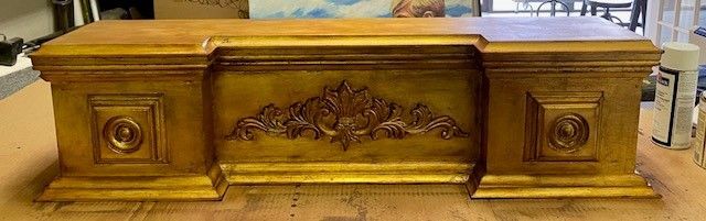 A golden-painted desk or console table with ornate detailing and a decorative floral element.