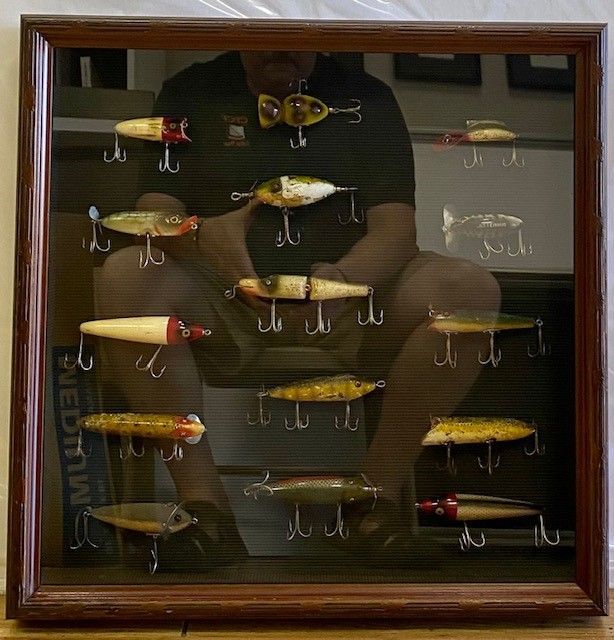 A collection of vintage fishing lures displayed in a wooden framed case.