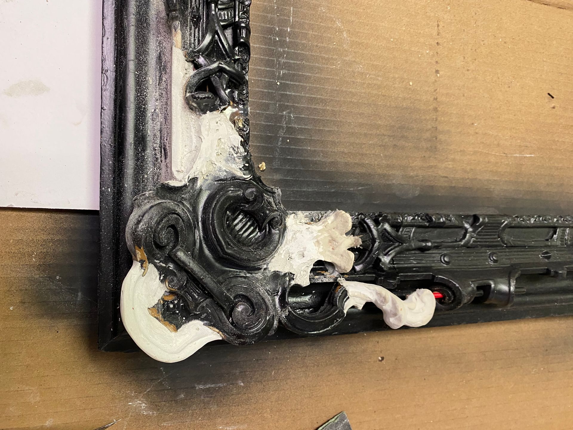 Close-up of a dark, ornate picture frame corner with white filler material applied to repair damage.