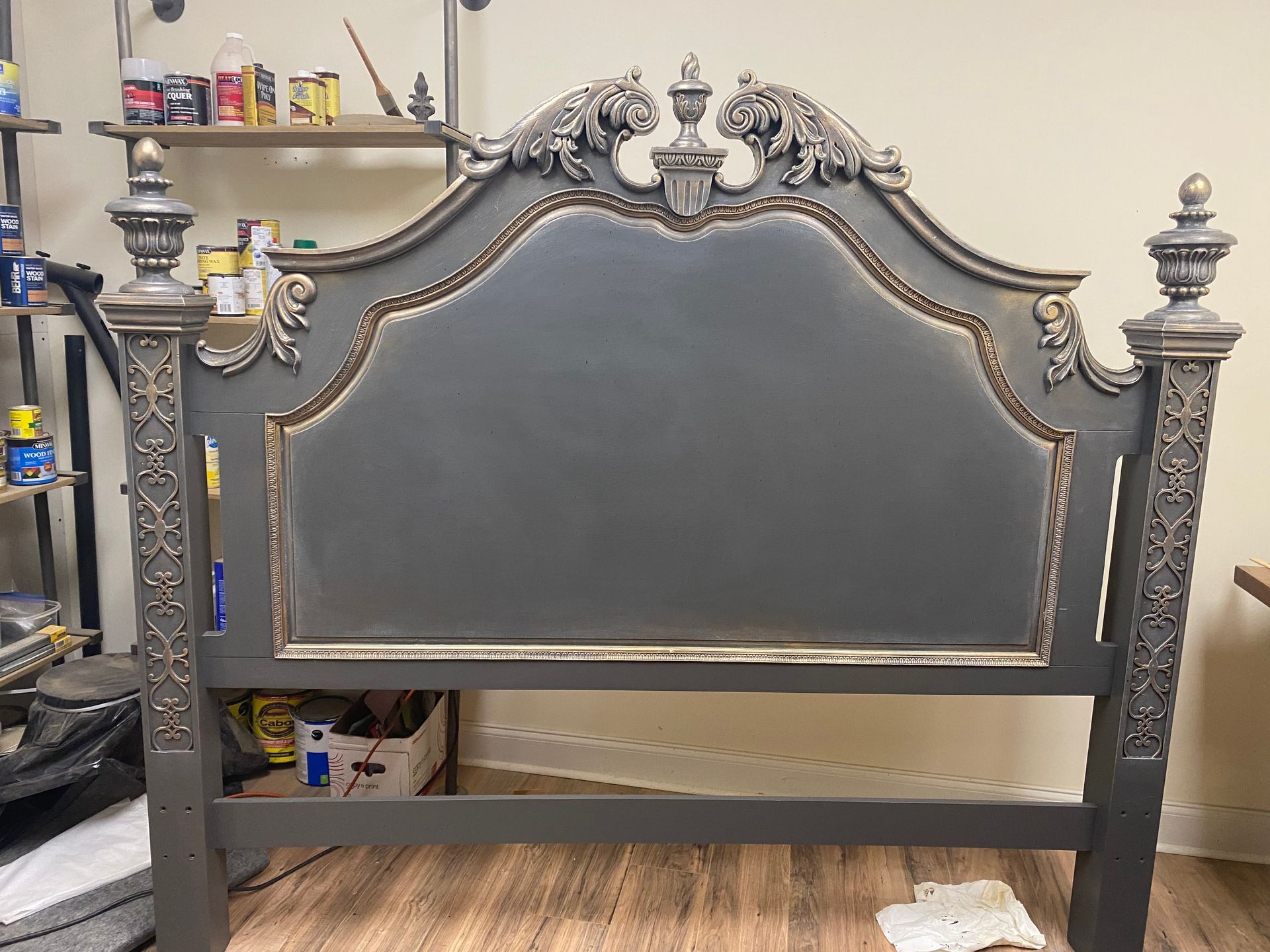 Gray and silver ornate headboard with carved details in a workshop setting. The headboard has a padded center.
