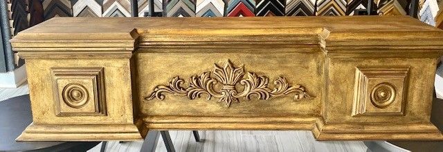 Gold-painted wooden mantelpiece with ornate carved details, in front of a variety of framed pictures.