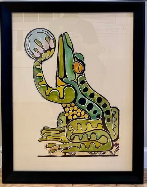 Green and yellow stylized frog holding a pale blue sphere with pink details, inside a black frame.