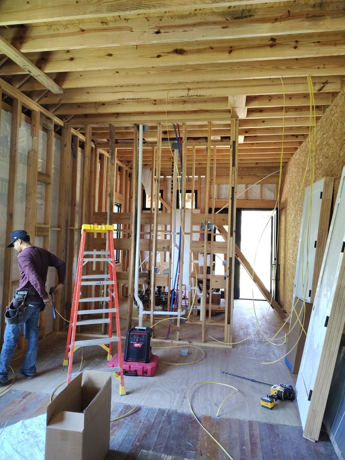 Construction site interior with exposed framing, ladders, tools, and two workers renovating a room