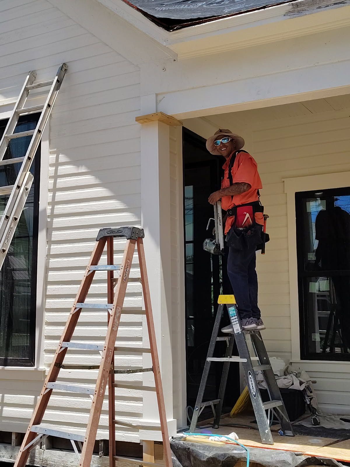 Worker on a ladder painting a white house exterior near a porch.