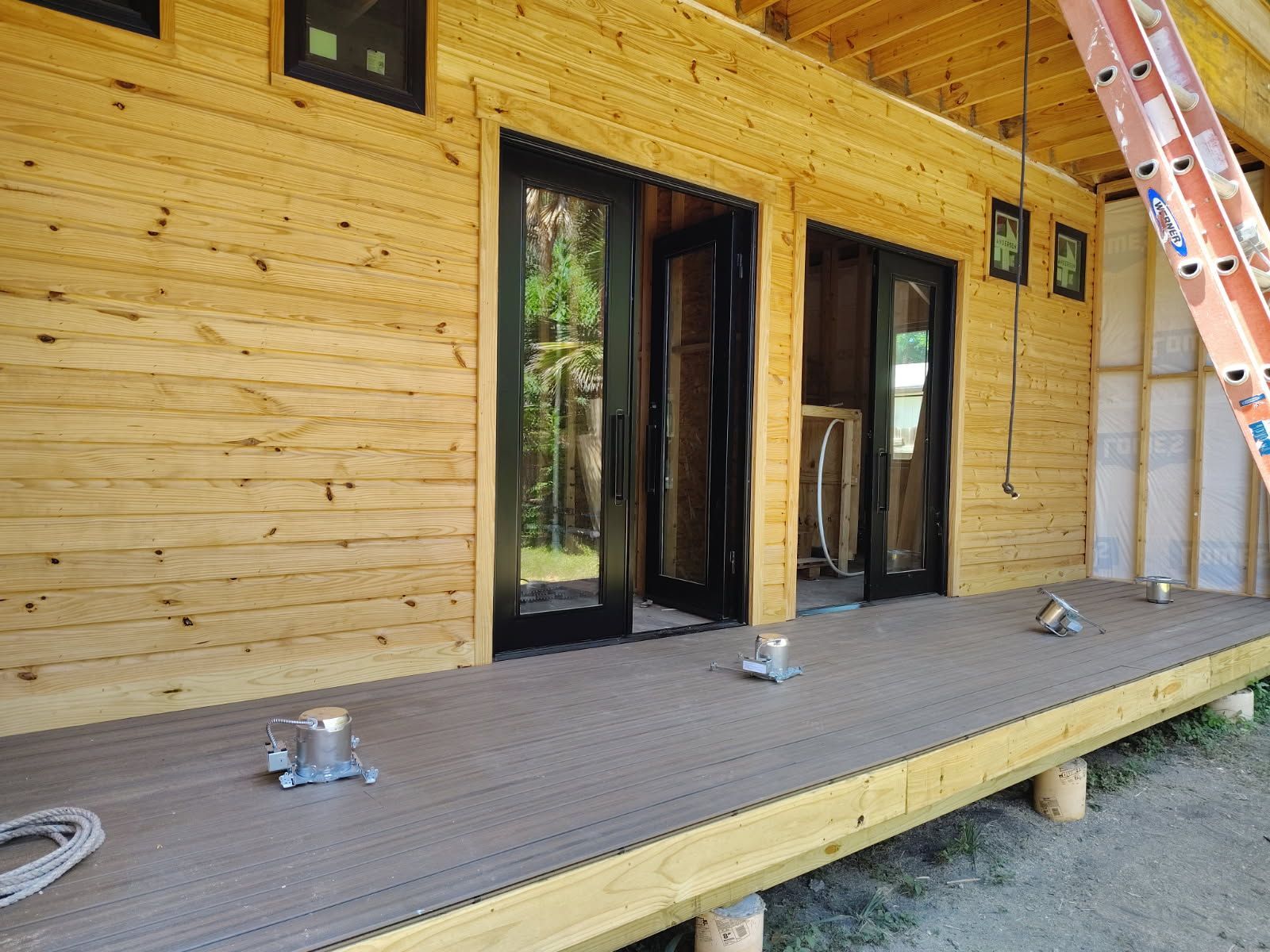 Wood-sided house exterior with unfinished porch, open doors, and a ladder leaning against the wall.