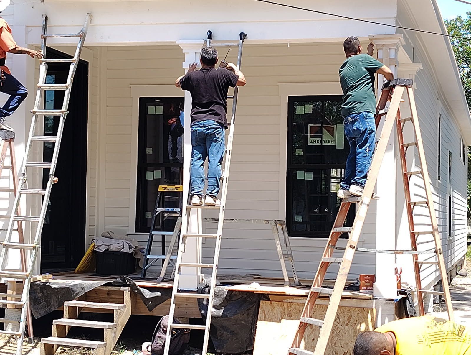 Workers painting a house exterior on ladders around the front porch