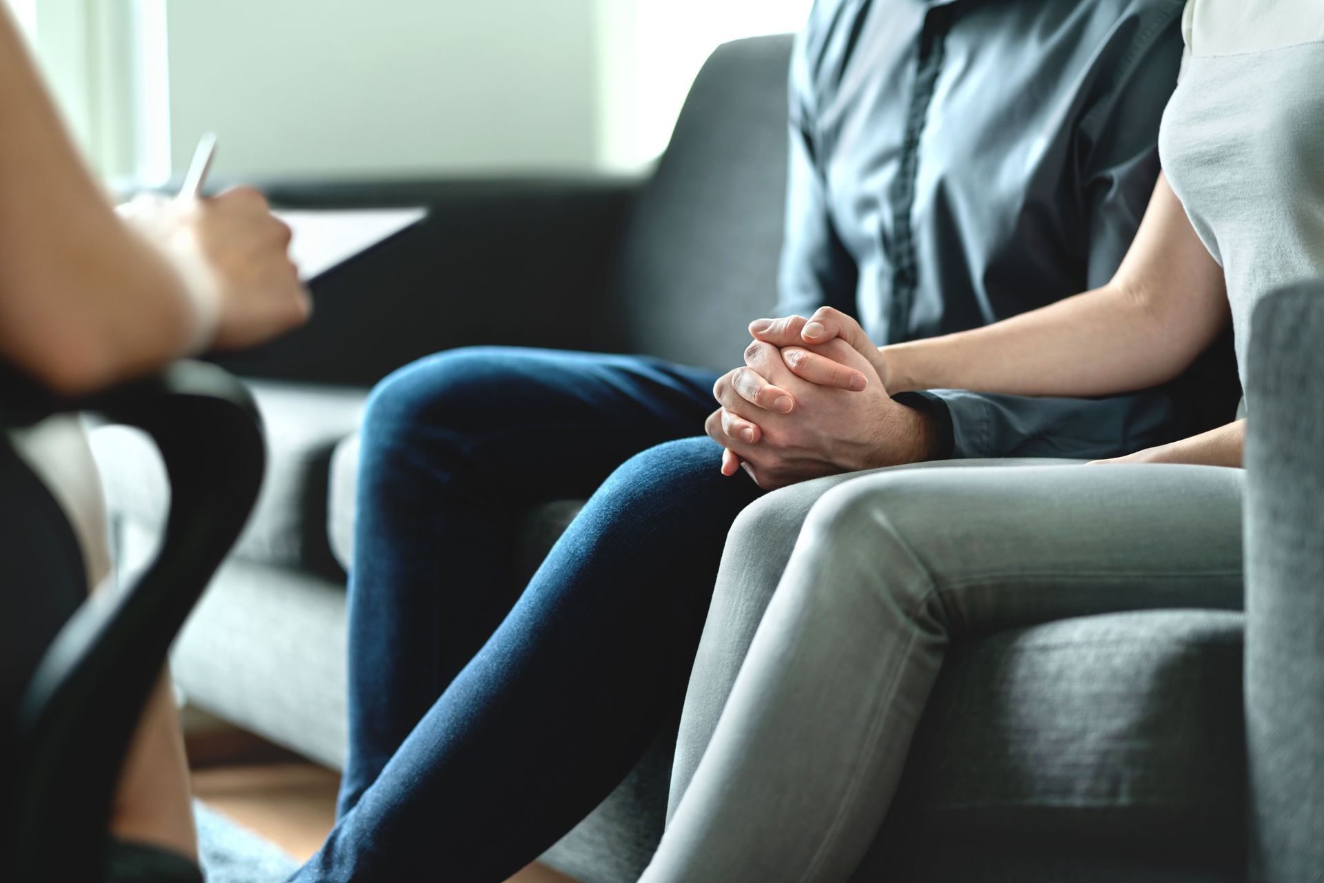 People seated on a couch in a counseling or discussion setting, hands clasped together