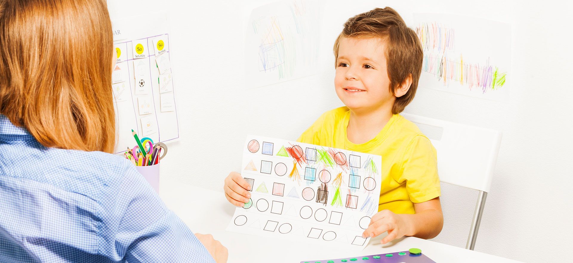 Teacher showing a child a colorful drawing in a bright classroom