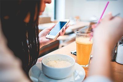 Person holding a smartphone at a café table with coffee, tea, and a bowl of soup