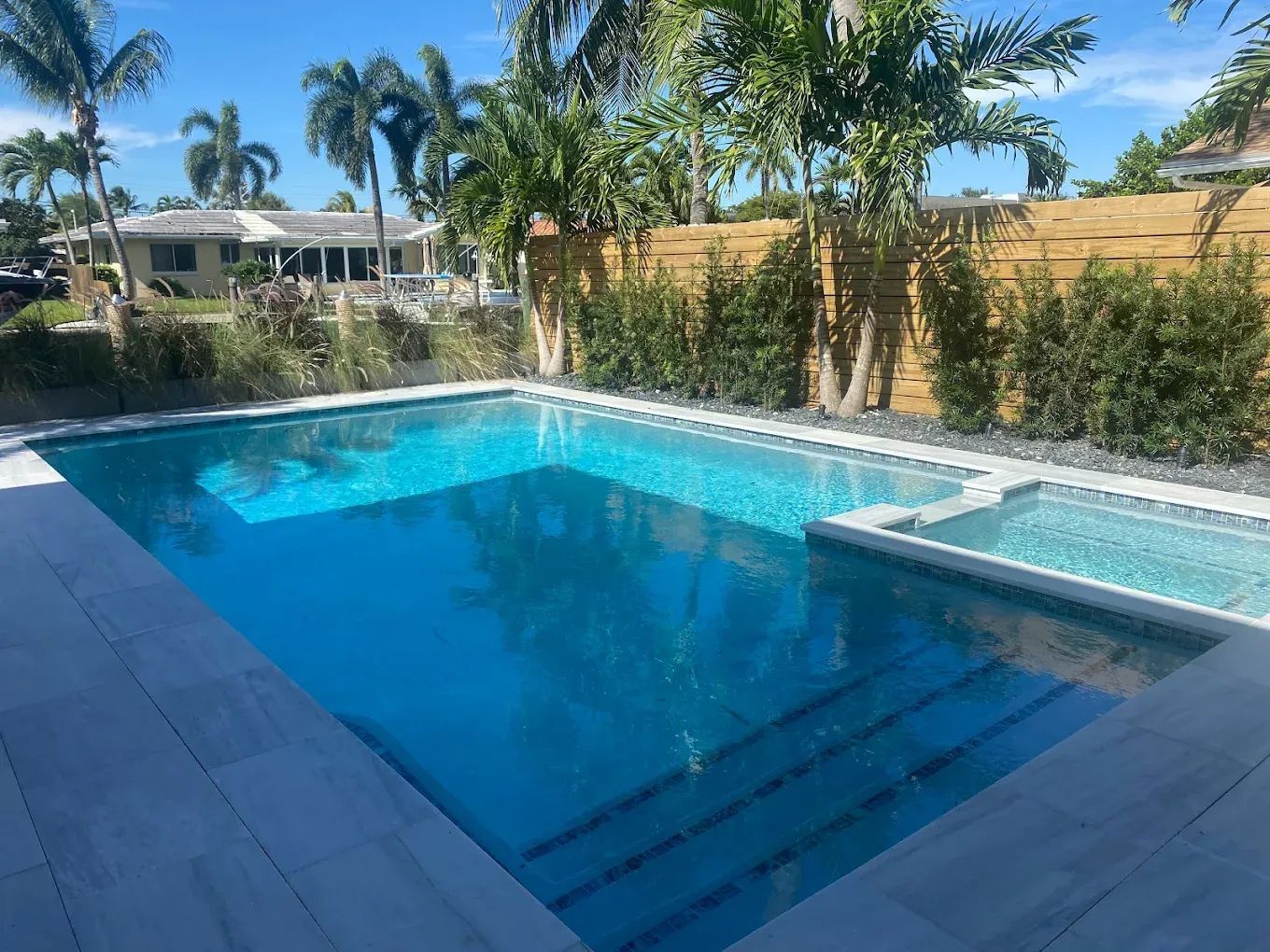 A large swimming pool in the backyard of a house surrounded by palm trees.