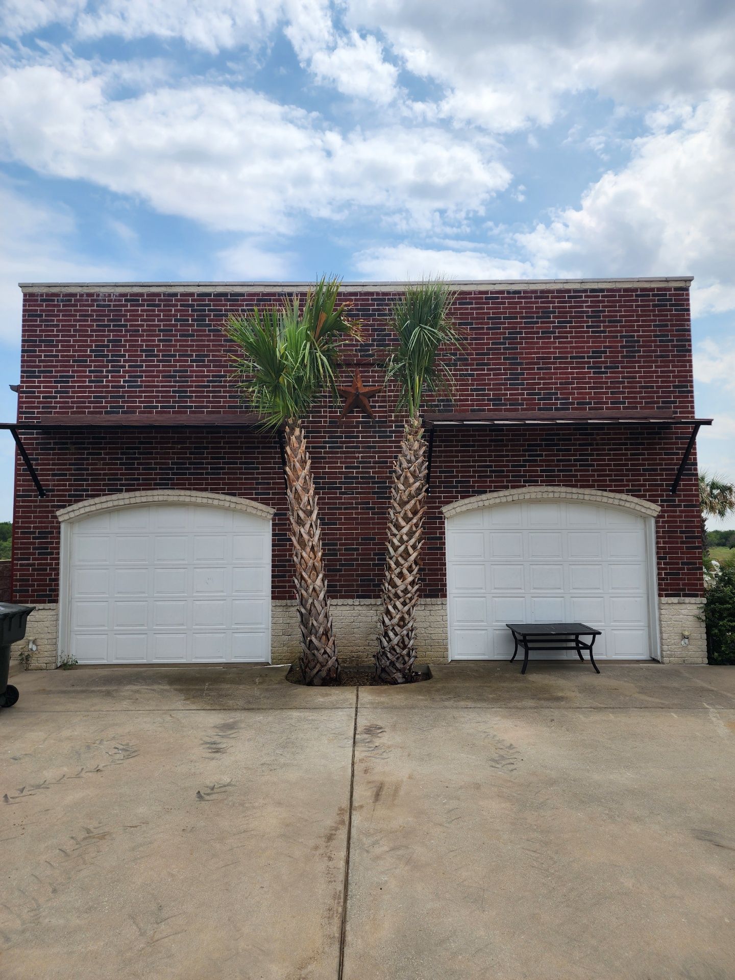A brick building with two white garage doors and palm trees