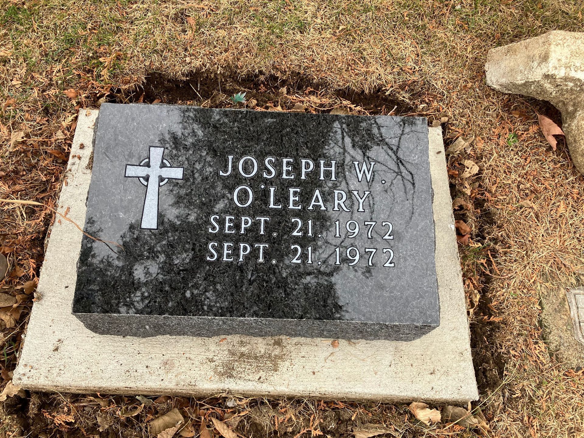 A black gravestone with a cross on it is in a cemetery