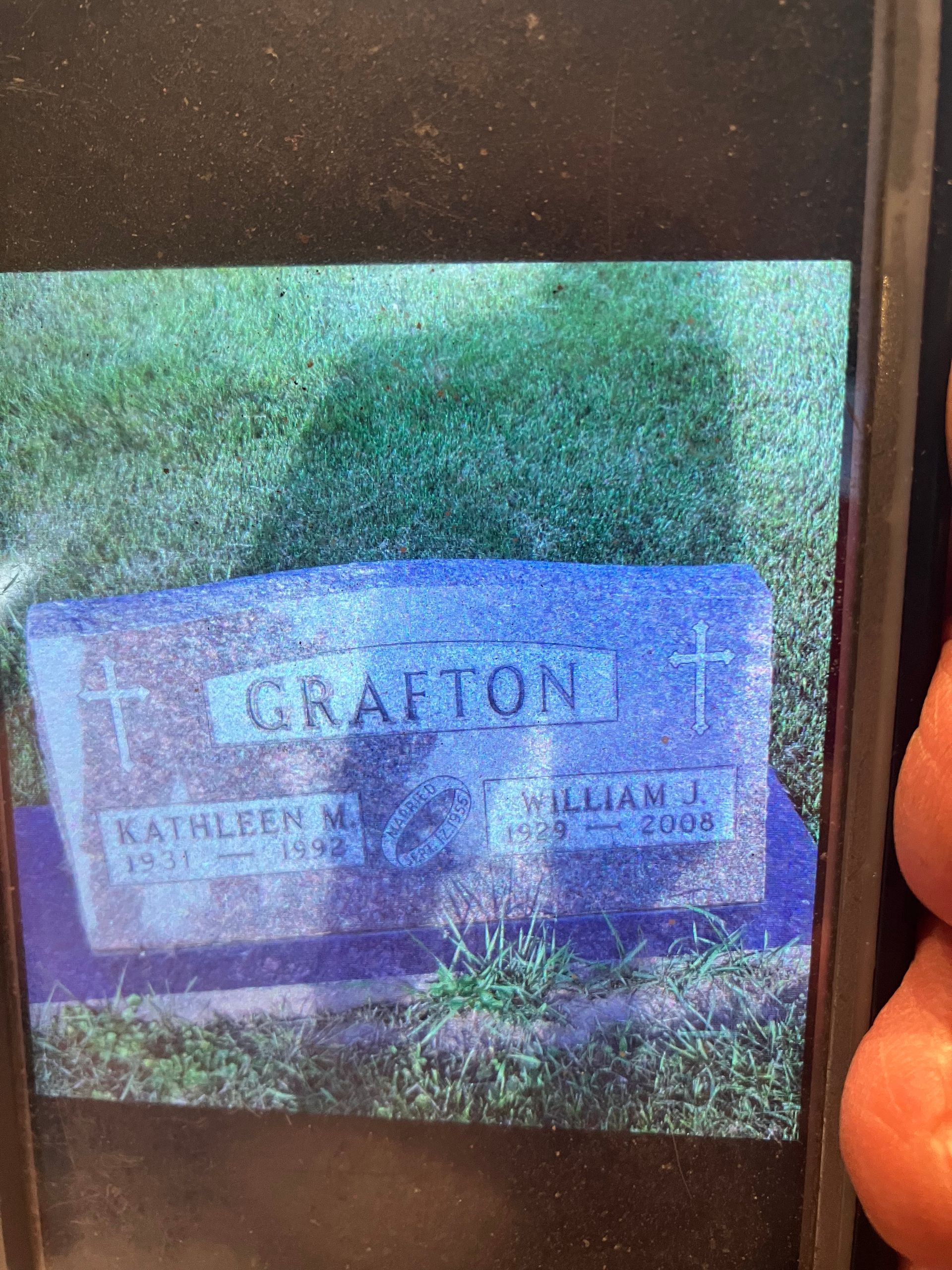 A person is holding a cell phone with a picture of a grave