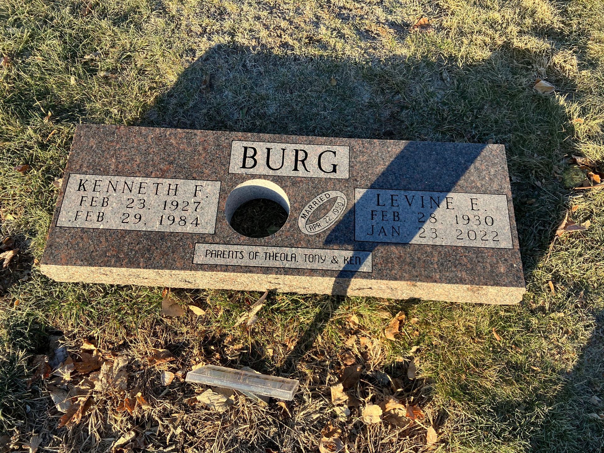 A gravestone with a hole in the middle of it is sitting on the ground in a cemetery