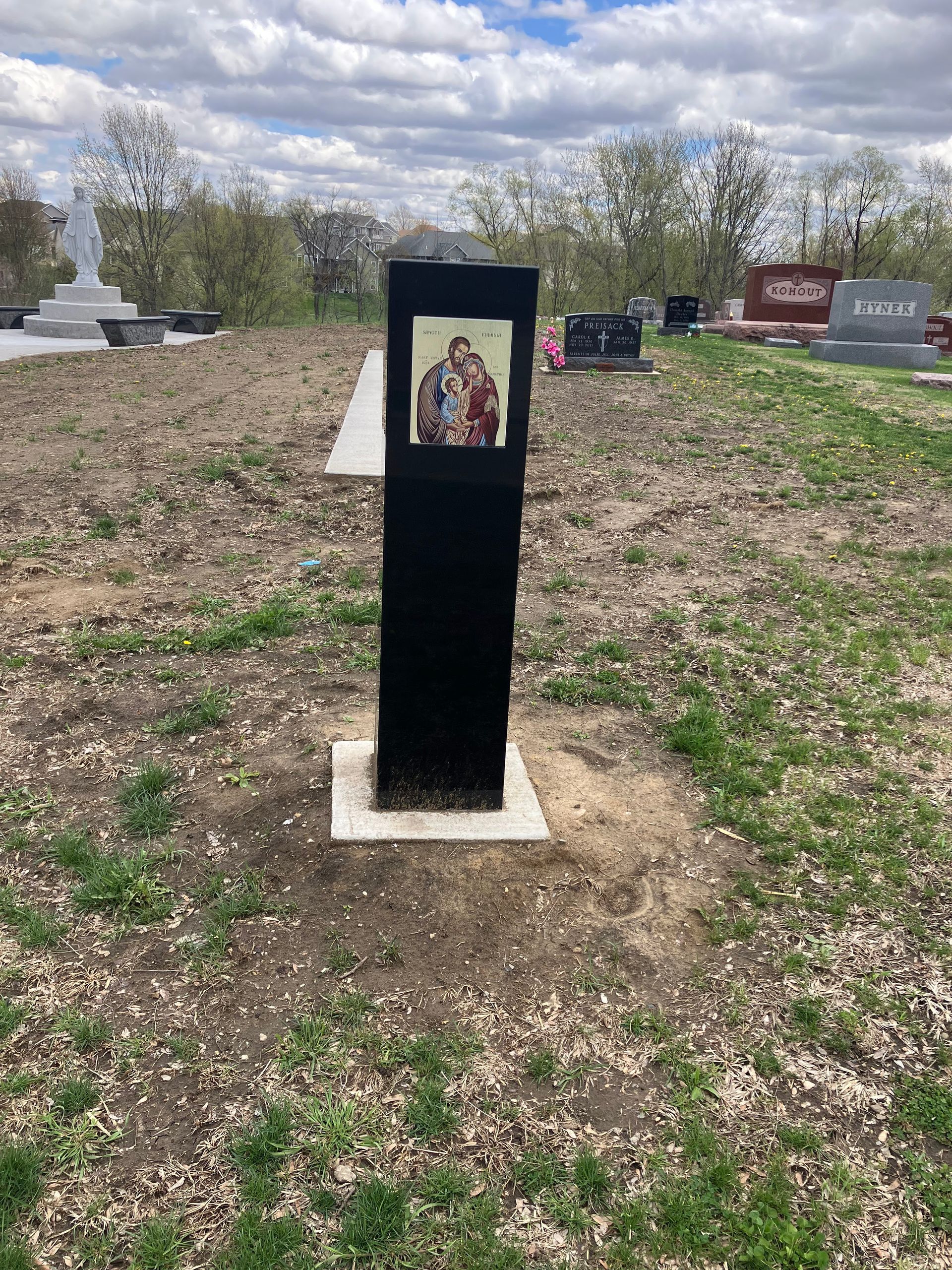 A black pole with a picture of Jesus and Mary on it in a cemetery