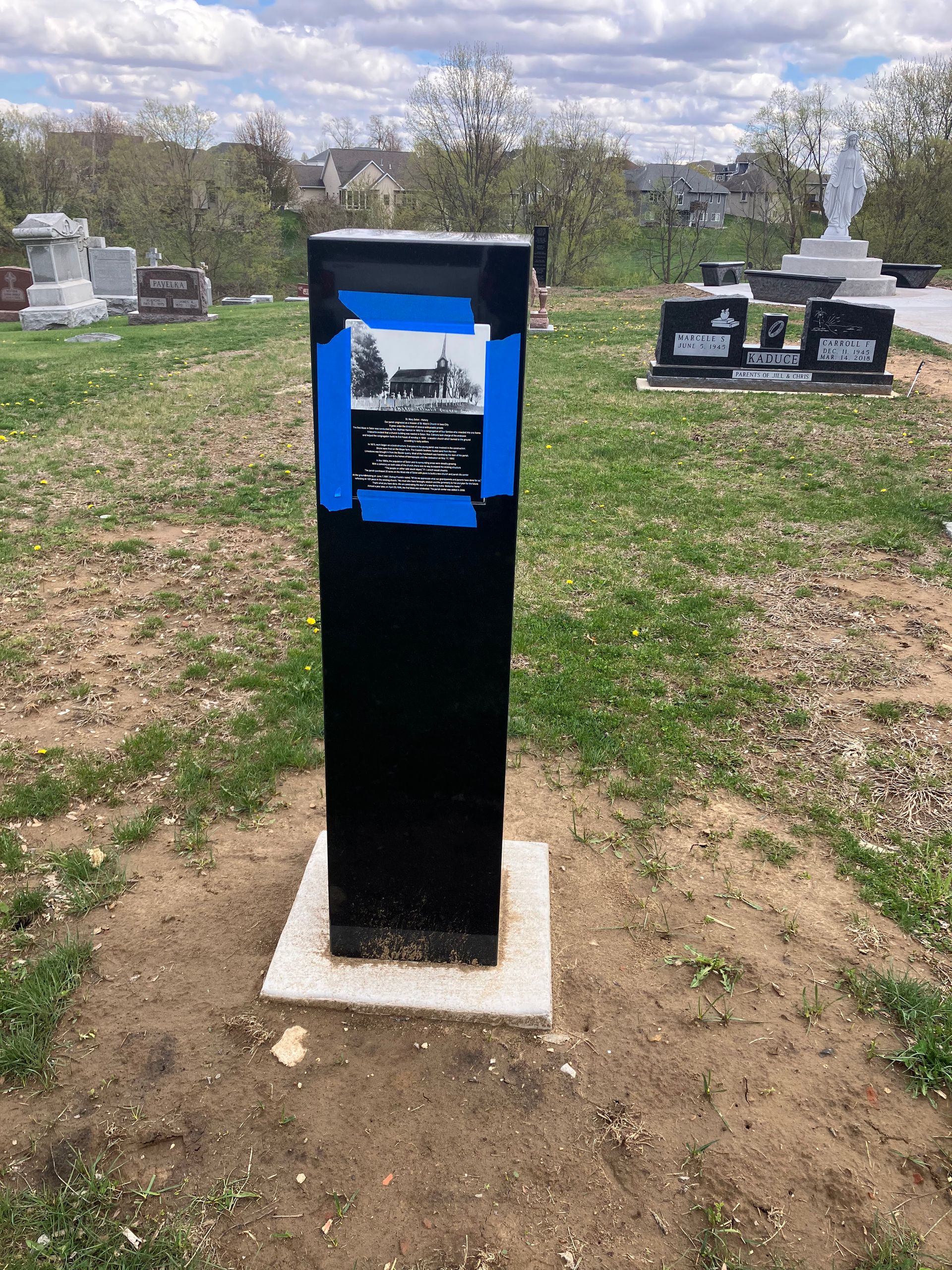 A black pole with a picture on it is in a cemetery