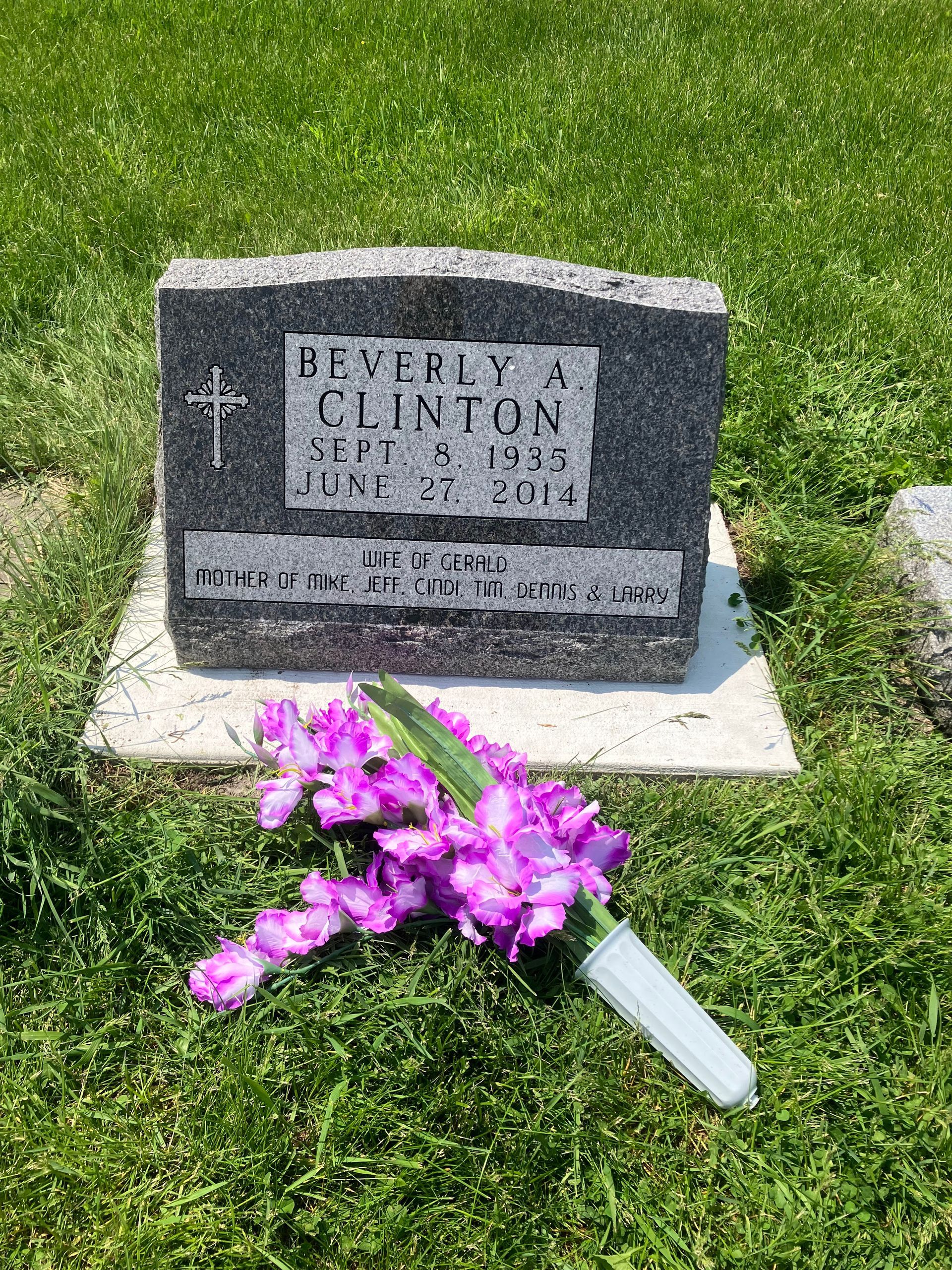 A gravestone with purple flowers in front of it in a cemetery