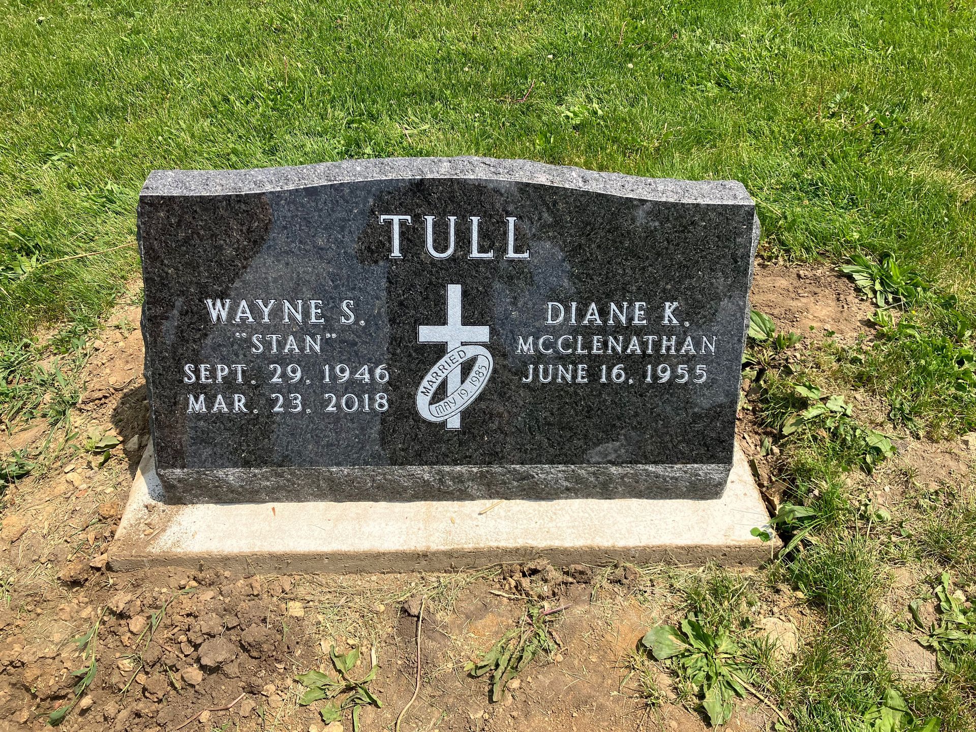 A black gravestone in a cemetery with a cross on it