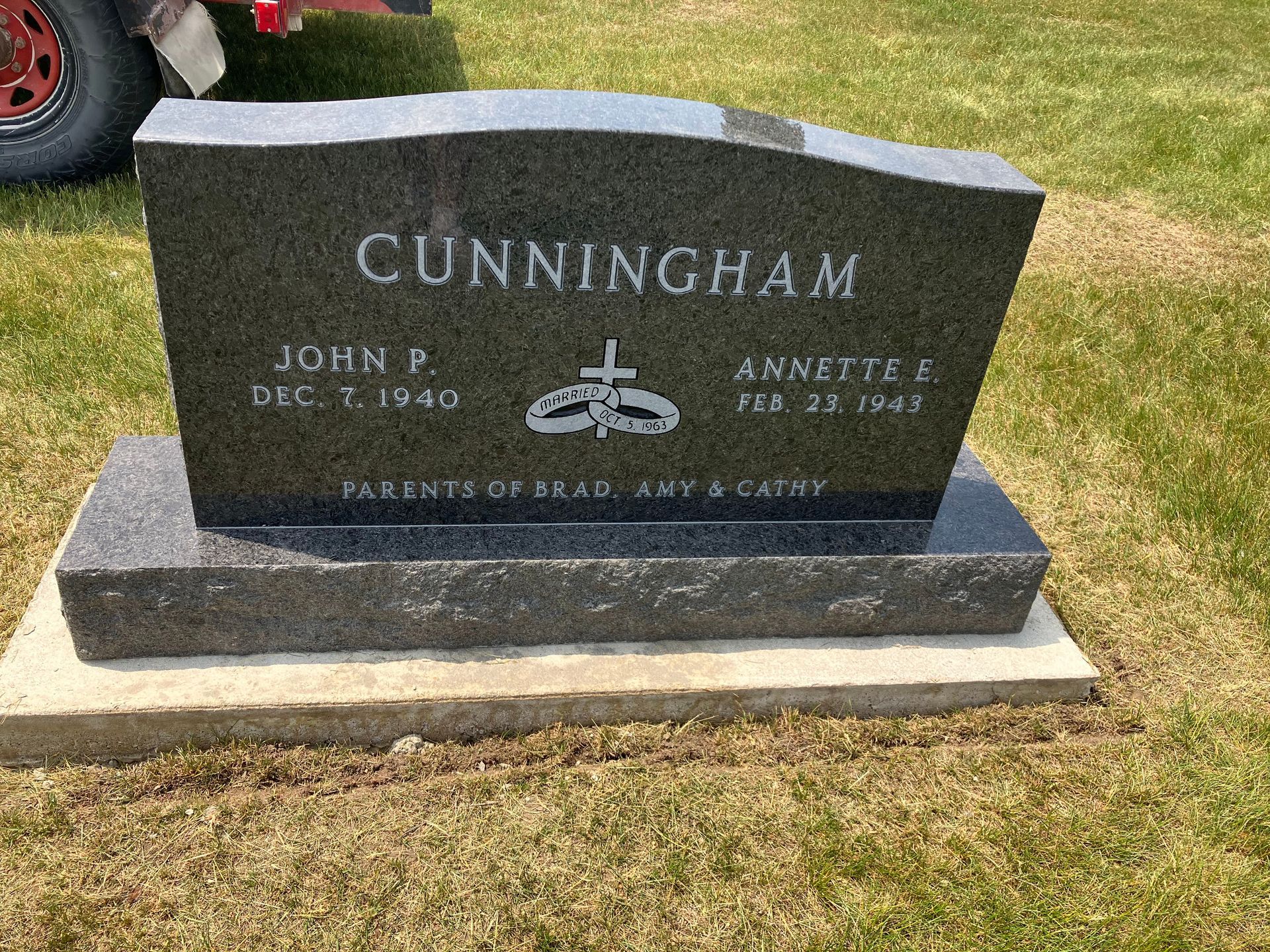 A black gravestone in a cemetery with a truck in the background