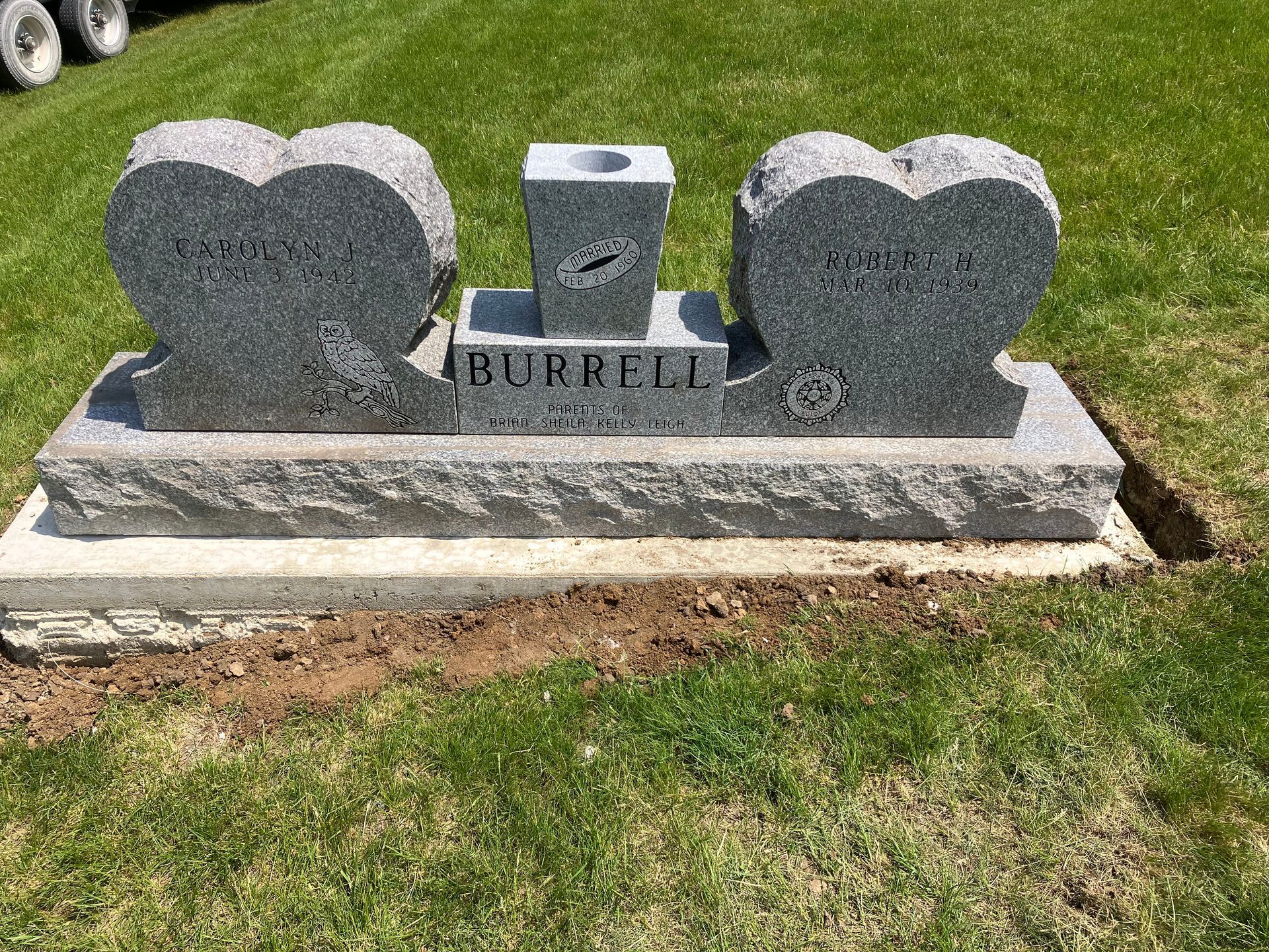 A gravestone with two hearts carved into it is in a cemetery