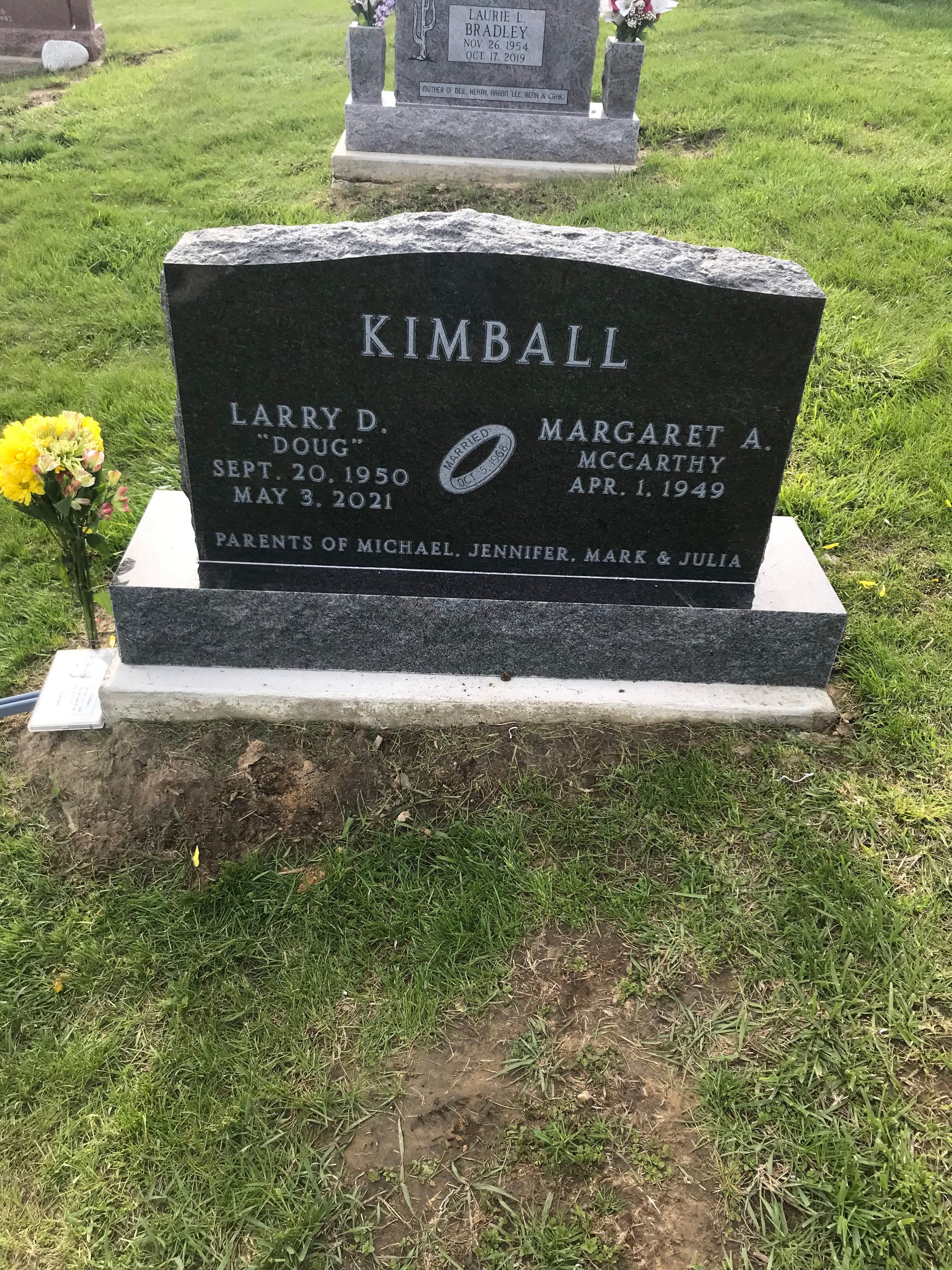 A black gravestone in a cemetery with a yellow flower in front of it