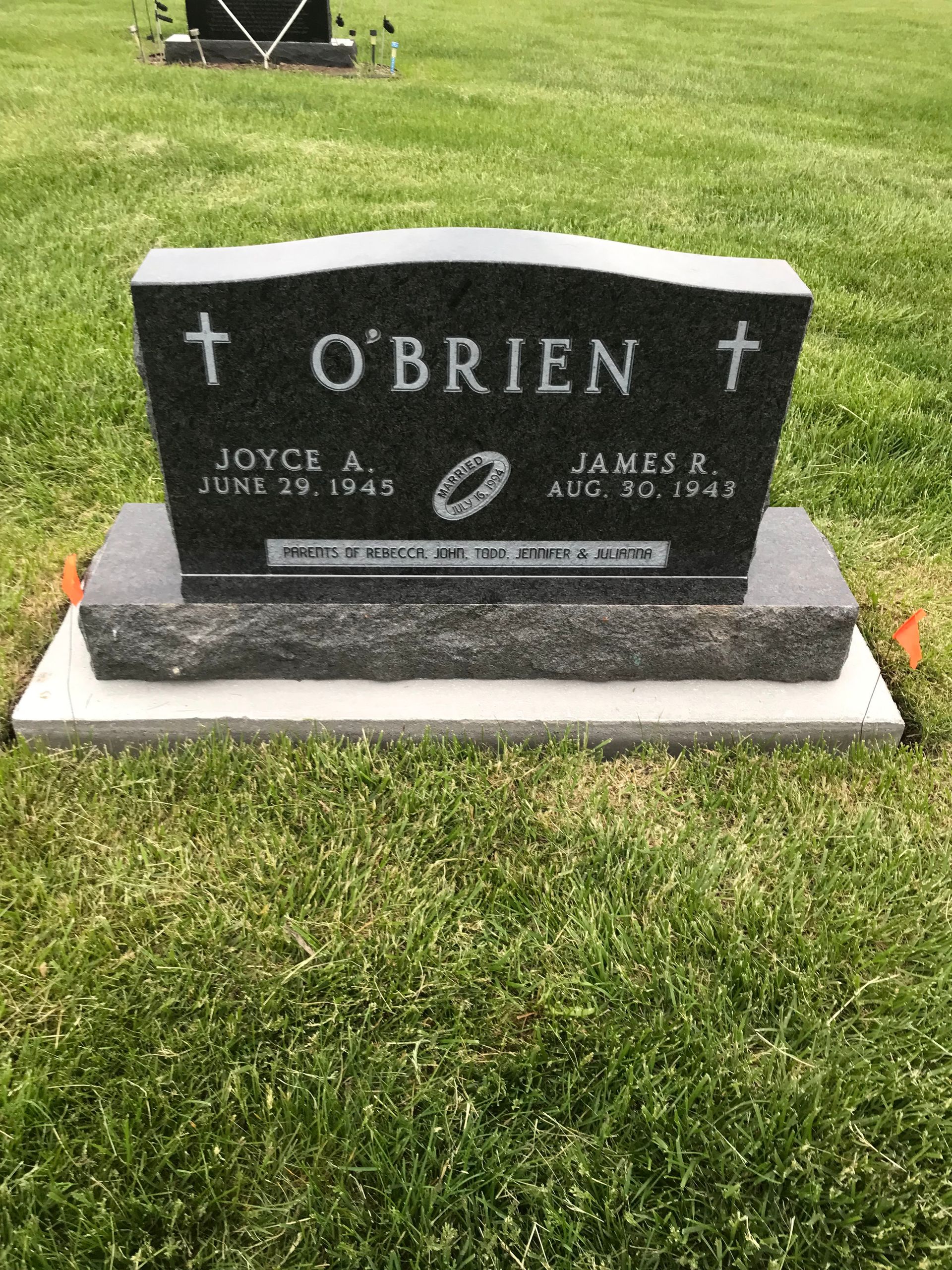 A black gravestone with a cross on it is in a cemetery